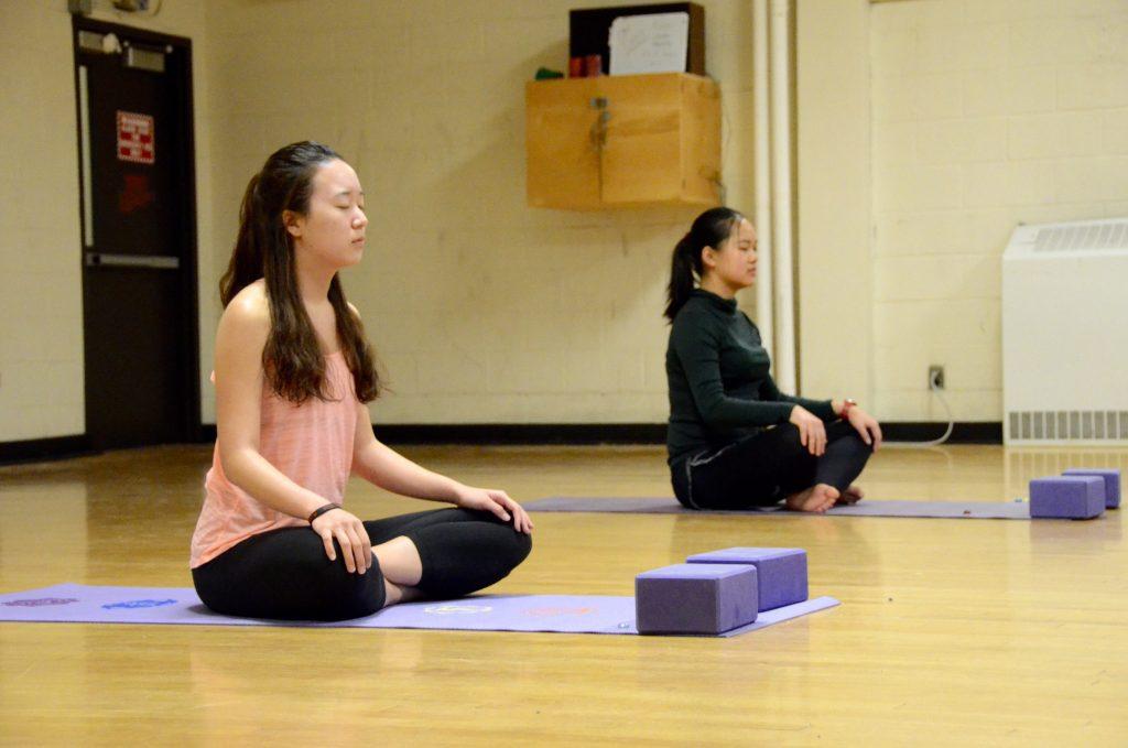 Two students doing yoga in gym.