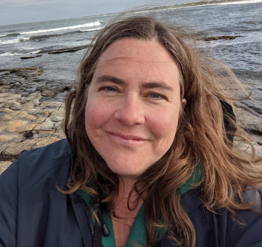 close-up of Tufts in London Assistant Director Vicky Hill with rocky ocean landscape in the background