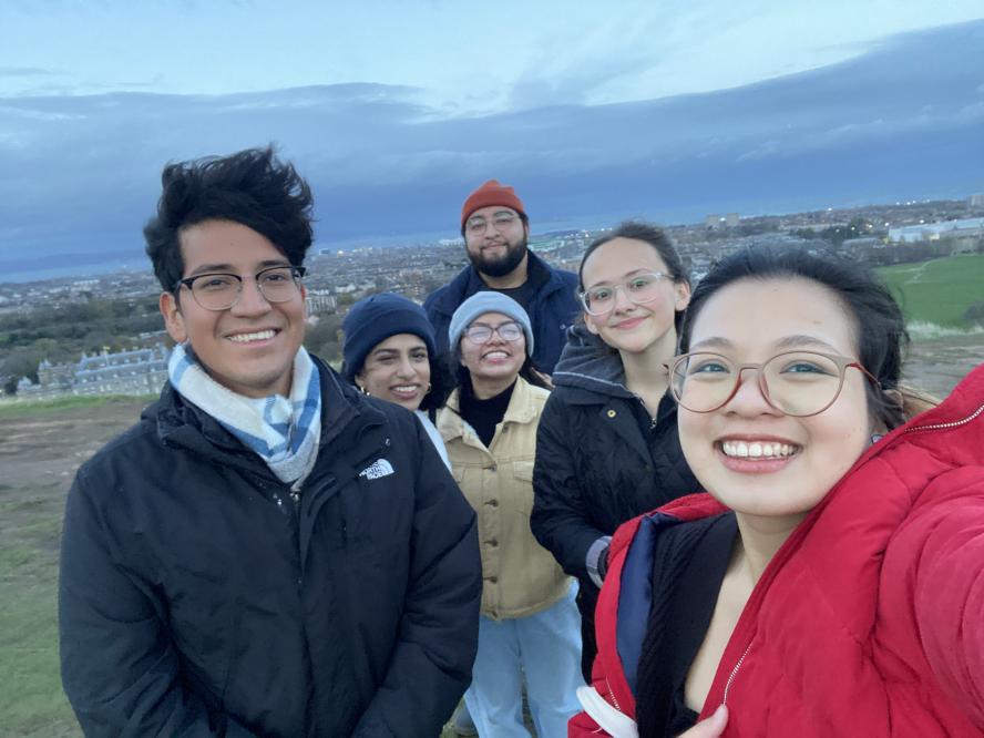 group of six students take selfie on top of a windy hill