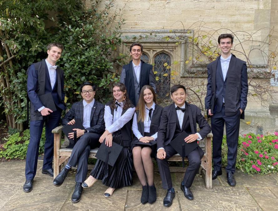 group of 7 students wearing suits pose in front of oxford building