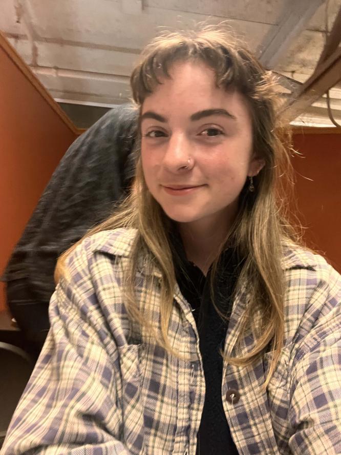 Coordinator Eleanor Tyne sitting in dining hall wearing flannel shirt smiling at the camera