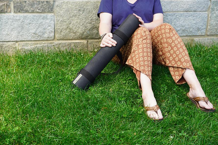 Person holding yoga mat sitting in grass