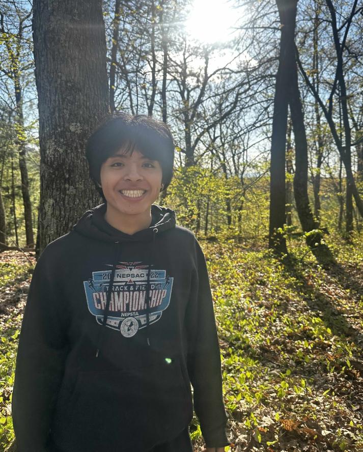 Coordinator Charlie smiling in the woods with the sun behind him wearing a black sweatshirt
