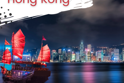 Boat with sails on water with Hong Kong skyline in the background at night with colorful lights.